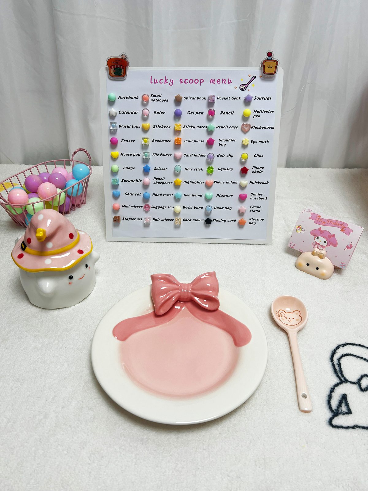 Lucky Scoop Mystery Box how to play scene with lucky scoop prize menu board listing cute stationery and toy prizes, pink bow plate, ceramic scoop spoon, basket of colorful balls and My Melody decor on fluffy white background